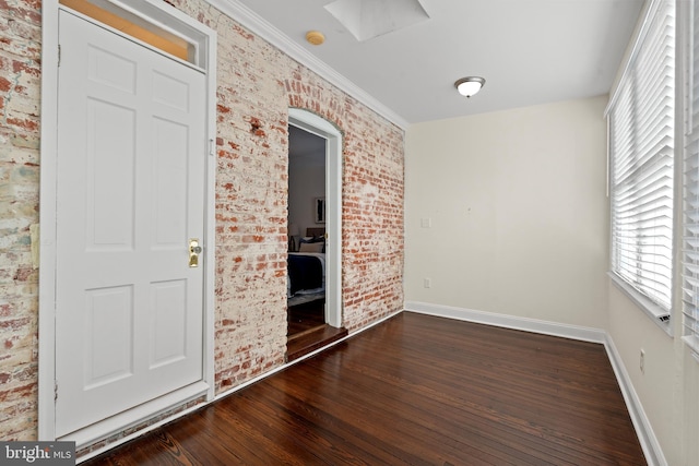 interior space featuring dark hardwood / wood-style floors, ornamental molding, and brick wall