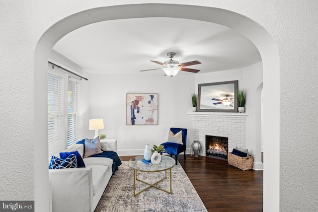 living room featuring dark hardwood / wood-style flooring, a brick fireplace, and ceiling fan