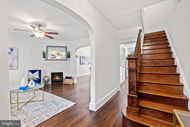 stairway with a brick fireplace, ceiling fan, and hardwood / wood-style flooring