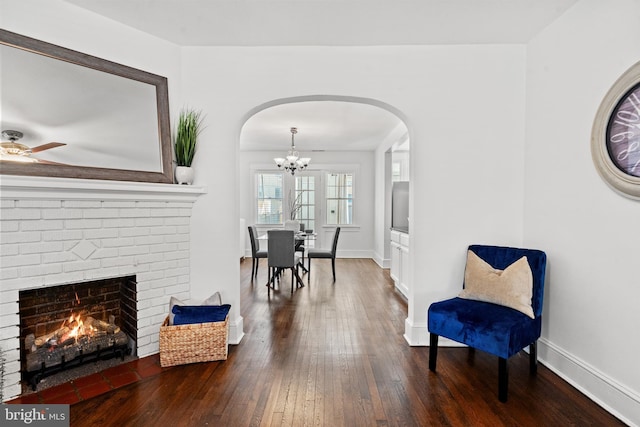 sitting room with ceiling fan with notable chandelier, dark hardwood / wood-style flooring, and a fireplace