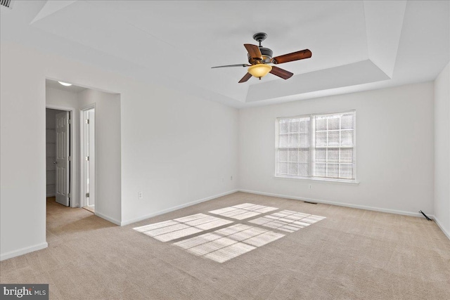 spare room with a raised ceiling, light colored carpet, and ceiling fan