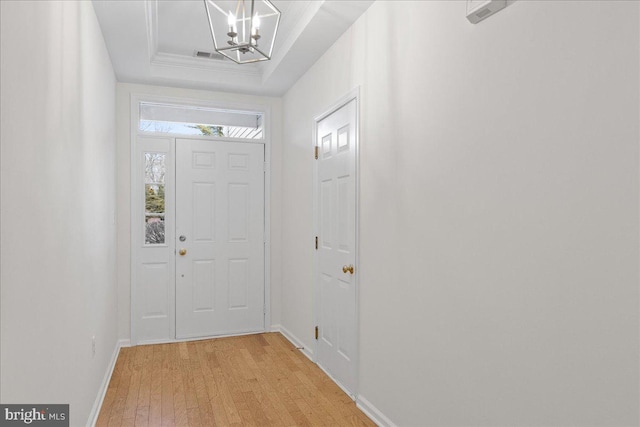 foyer featuring crown molding, light hardwood / wood-style flooring, a notable chandelier, and a tray ceiling