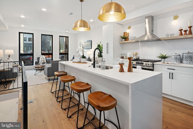 kitchen with light wood-type flooring, wall chimney exhaust hood, stainless steel gas range, pendant lighting, and white cabinets