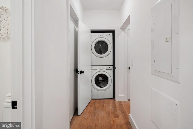 washroom featuring electric panel, stacked washer / drying machine, and light wood-type flooring