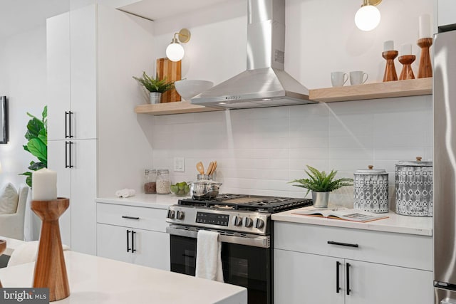 kitchen with tasteful backsplash, white cabinets, wall chimney range hood, and appliances with stainless steel finishes