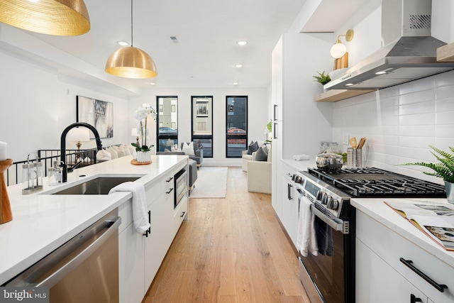 kitchen with decorative light fixtures, stainless steel appliances, white cabinetry, and wall chimney range hood