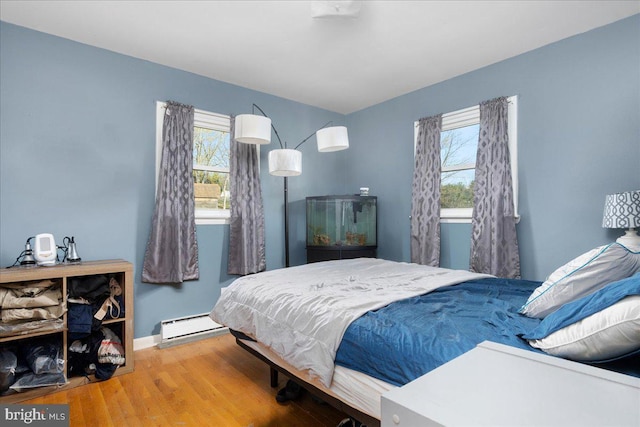 bedroom featuring wood-type flooring, multiple windows, and a baseboard heating unit