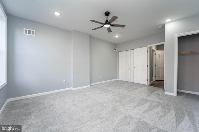 unfurnished bedroom featuring two closets, light colored carpet, and ceiling fan