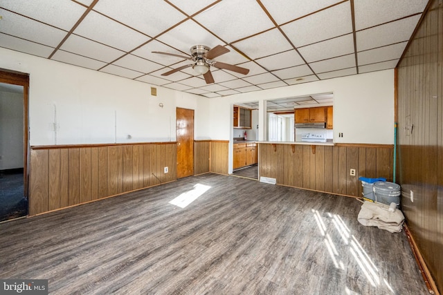 interior space with a paneled ceiling, dark hardwood / wood-style flooring, ceiling fan, and wooden walls