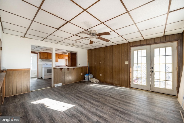 unfurnished living room featuring dark hardwood / wood-style floors, wood walls, ceiling fan, and french doors