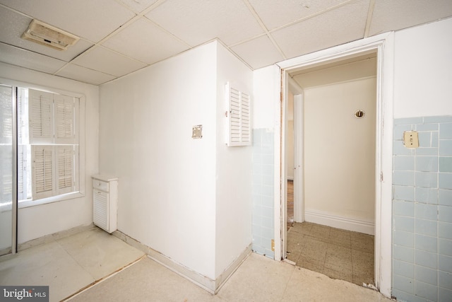 corridor with a drop ceiling and tile walls