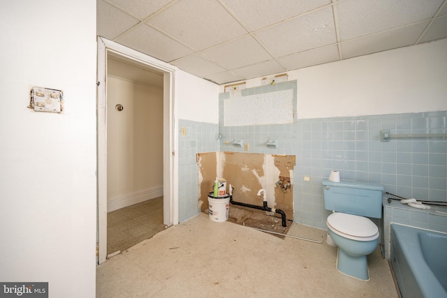 bathroom featuring a paneled ceiling, a tub to relax in, toilet, and tile walls