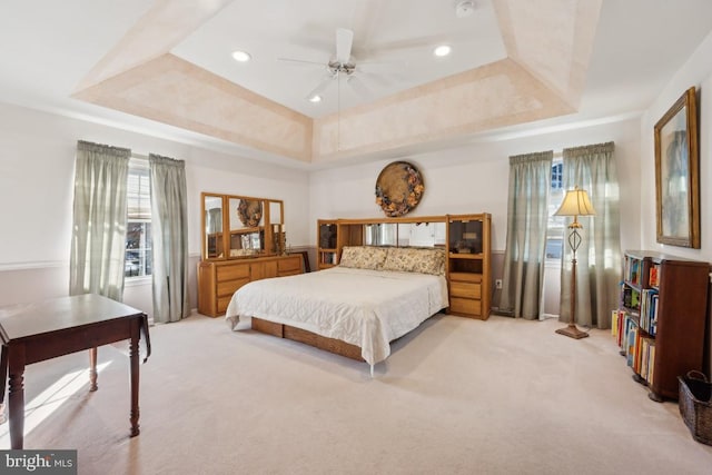 bedroom featuring a raised ceiling, light carpet, and ceiling fan