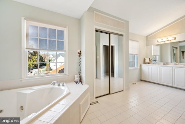 bathroom featuring tiled tub, tile patterned flooring, vanity, and lofted ceiling