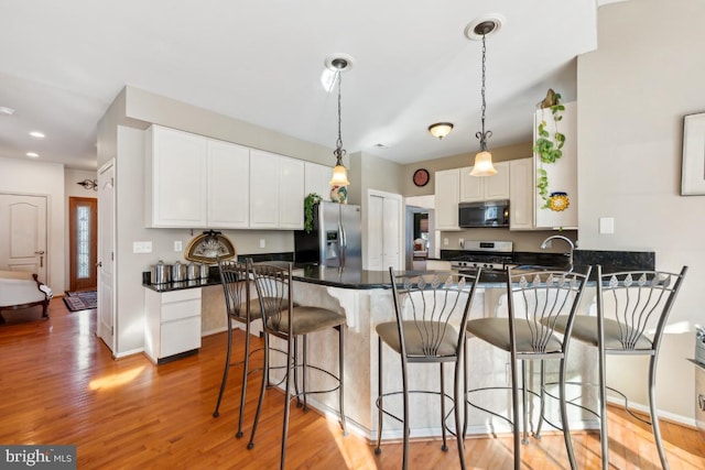 kitchen with pendant lighting, light wood-type flooring, appliances with stainless steel finishes, a kitchen bar, and white cabinetry