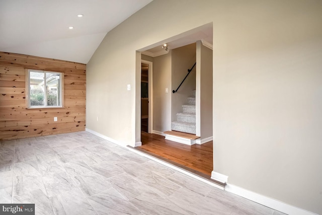 spare room featuring wood walls, light wood-type flooring, and vaulted ceiling