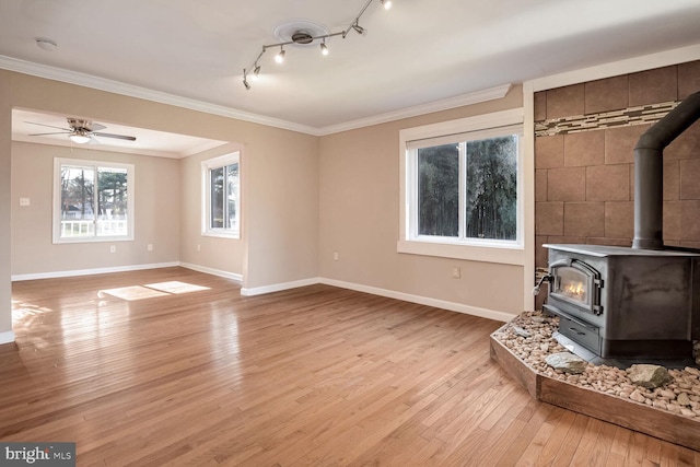 unfurnished living room featuring ceiling fan, light wood-type flooring, a wood stove, and ornamental molding