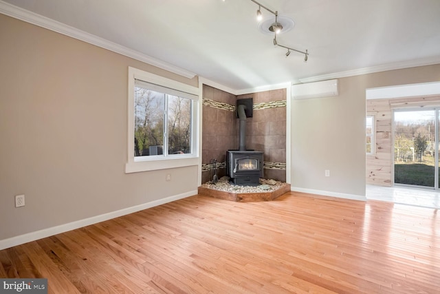 unfurnished living room with a wood stove, a wall unit AC, hardwood / wood-style floors, track lighting, and ornamental molding