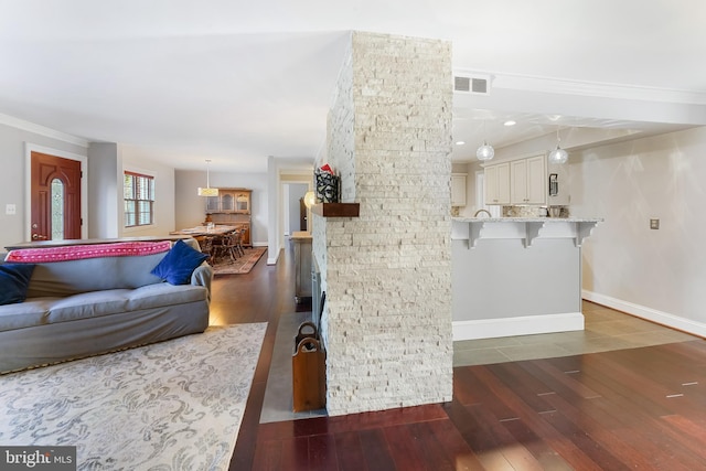 interior space featuring light stone countertops, ornamental molding, decorative light fixtures, dark hardwood / wood-style flooring, and a breakfast bar area