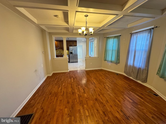 unfurnished dining area featuring beam ceiling, hardwood / wood-style floors, a chandelier, and coffered ceiling