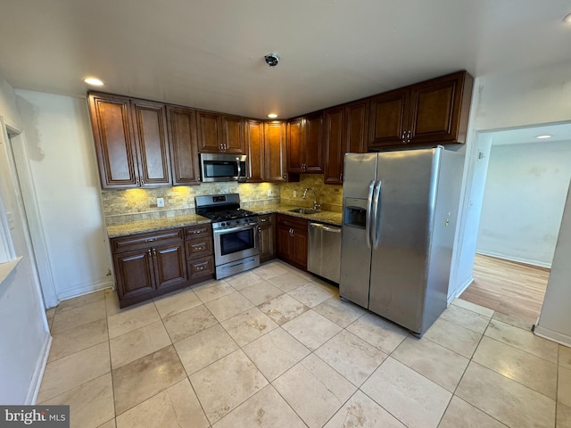 kitchen with sink, stainless steel appliances, light stone counters, light hardwood / wood-style floors, and decorative backsplash