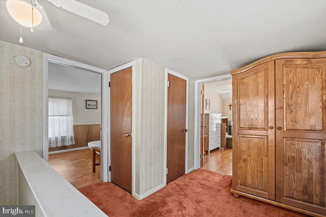 hallway featuring wooden walls, light hardwood / wood-style floors, and lofted ceiling