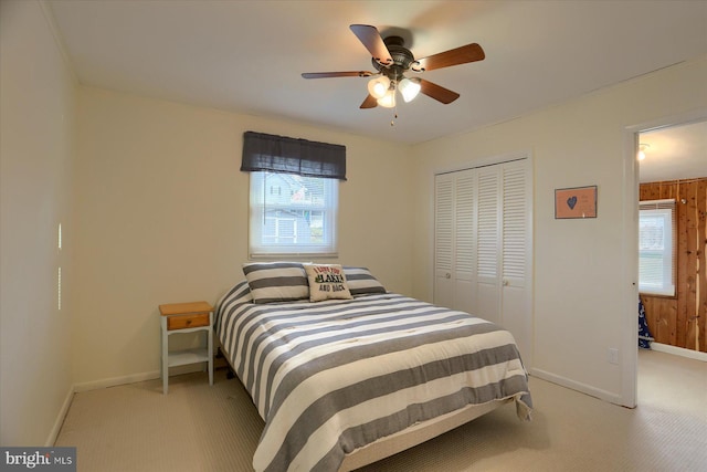 bedroom with multiple windows, ceiling fan, a closet, and wood walls