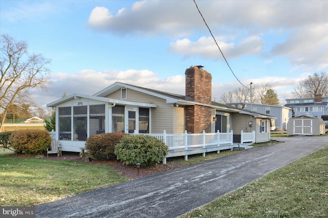 back of property featuring a yard, a deck, a storage unit, and a sunroom