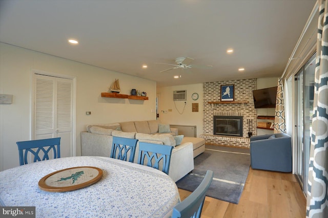 dining space featuring a fireplace, light hardwood / wood-style flooring, ceiling fan, and a wall unit AC