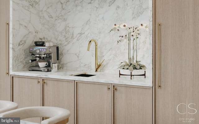 bar with light stone countertops, light brown cabinets, and sink