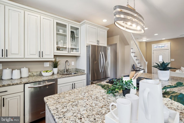 kitchen with appliances with stainless steel finishes, light stone counters, sink, pendant lighting, and white cabinets