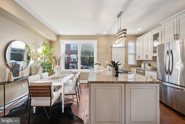 kitchen with dark wood-type flooring, white cabinets, hanging light fixtures, appliances with stainless steel finishes, and light stone counters