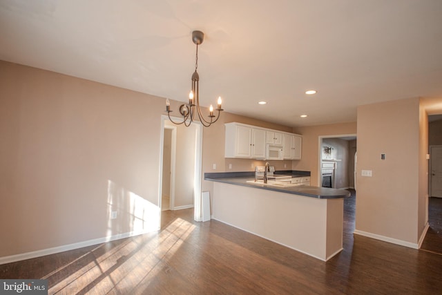 kitchen featuring dark wood-type flooring, an inviting chandelier, kitchen peninsula, decorative light fixtures, and white cabinetry