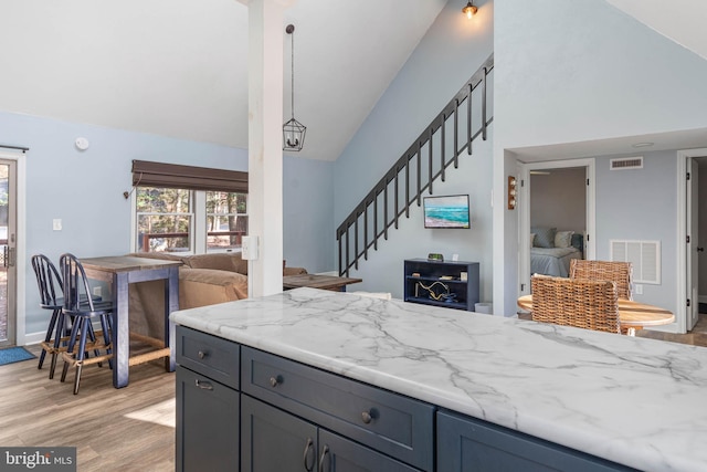 kitchen with light stone countertops, an inviting chandelier, high vaulted ceiling, pendant lighting, and light hardwood / wood-style floors