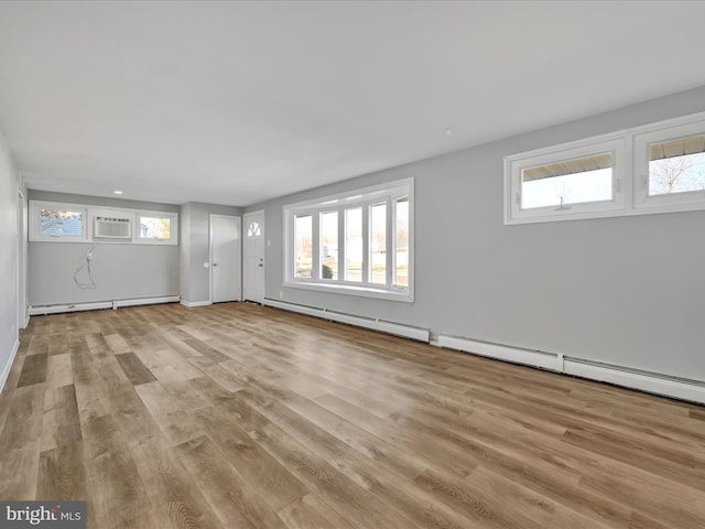 basement with a wealth of natural light, light hardwood / wood-style flooring, and a baseboard radiator