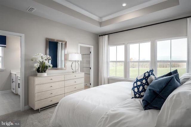 carpeted bedroom featuring a raised ceiling, ensuite bath, and ornamental molding