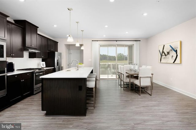 kitchen with stainless steel appliances, hanging light fixtures, a center island with sink, and light hardwood / wood-style floors