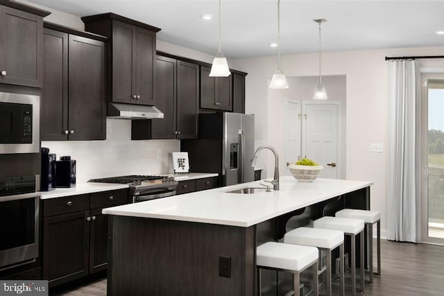 kitchen with stainless steel appliances, a center island with sink, pendant lighting, and wood-type flooring