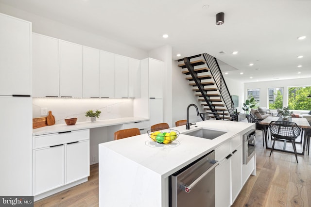 kitchen with dishwasher, sink, light hardwood / wood-style flooring, a center island with sink, and white cabinets