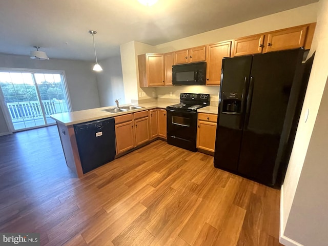 kitchen with kitchen peninsula, sink, black appliances, light hardwood / wood-style floors, and hanging light fixtures