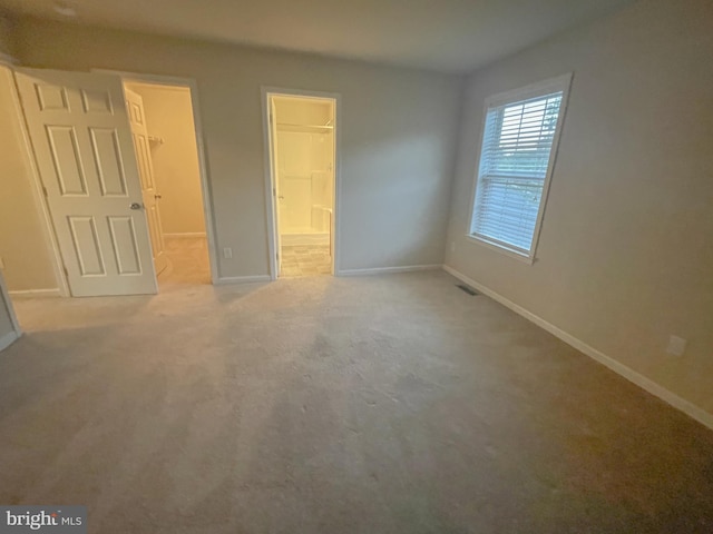 unfurnished bedroom with light colored carpet, a spacious closet, and a closet