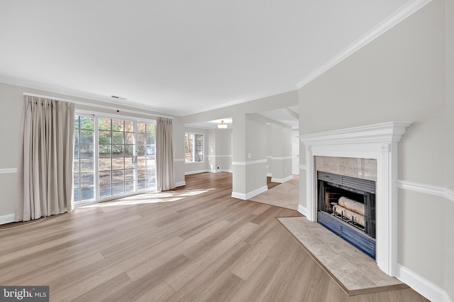 unfurnished living room with light hardwood / wood-style flooring, ornamental molding, and a tiled fireplace