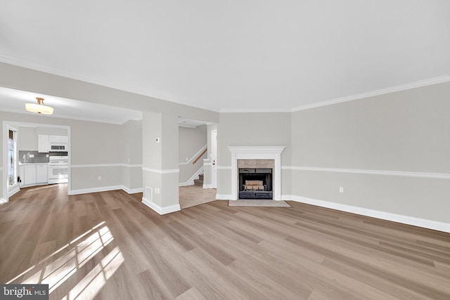 unfurnished living room with a tiled fireplace, light hardwood / wood-style floors, and ornamental molding