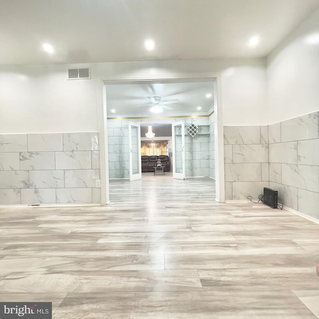 unfurnished living room featuring ceiling fan and tile walls