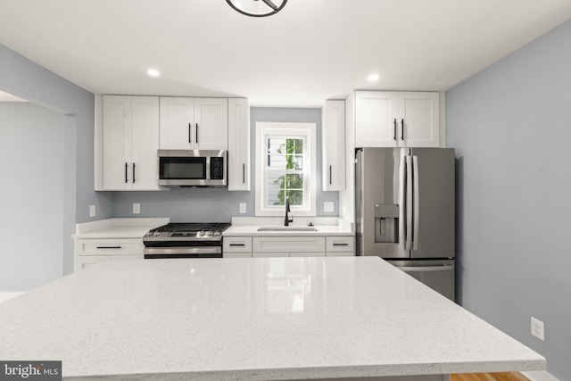 kitchen featuring white cabinets, appliances with stainless steel finishes, light stone countertops, and sink