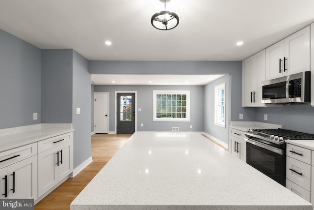 kitchen featuring white cabinets, light hardwood / wood-style floors, light stone counters, and appliances with stainless steel finishes