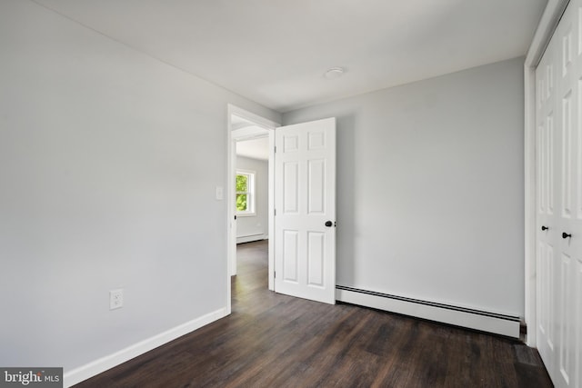 unfurnished bedroom with a closet, baseboard heating, and dark wood-type flooring