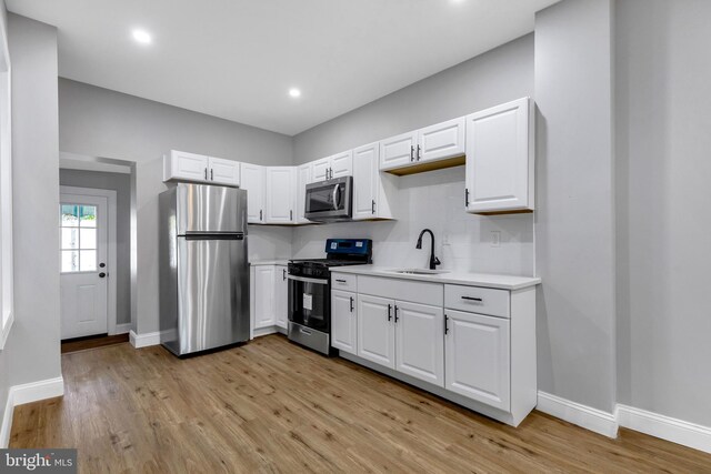 kitchen featuring sink, light wood-type flooring, appliances with stainless steel finishes, tasteful backsplash, and white cabinetry