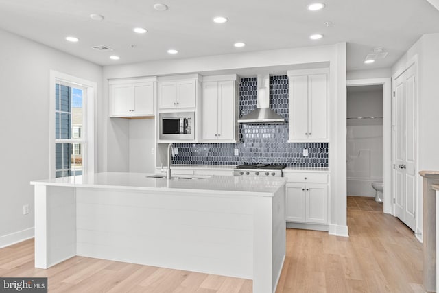 kitchen featuring a kitchen island with sink, built in microwave, wall chimney exhaust hood, and sink