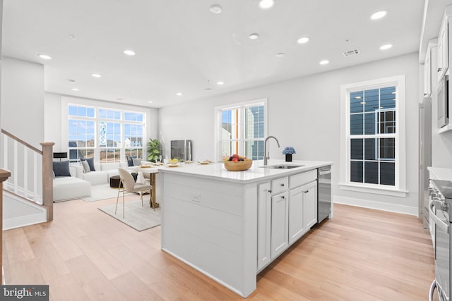 kitchen with white cabinets, light wood-type flooring, sink, and an island with sink